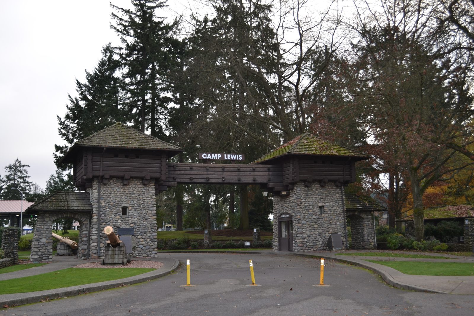 The stone and log Camp Lewis arch gate at Joint Base Lewis-McChord with two cannons and yellow bollards