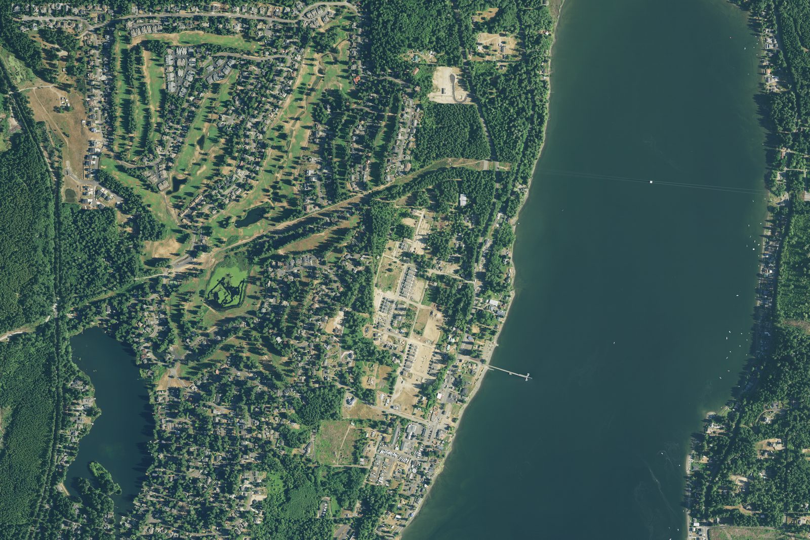 Aerial photo of Allyn: LakeLand Village homes wrapped around the golf course and Lake Anderson, SR-3 running through town, and the Port of Allyn pier reaching into North Bay on Case Inlet
