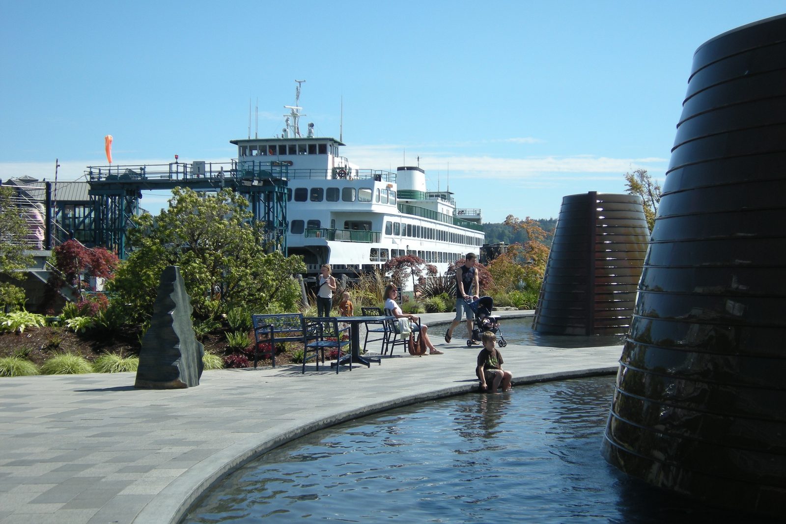 Washington State Ferry docked at Harborside Fountain Park in downtown Bremerton, with visitors around the fountain and the boardwalk buildings behind