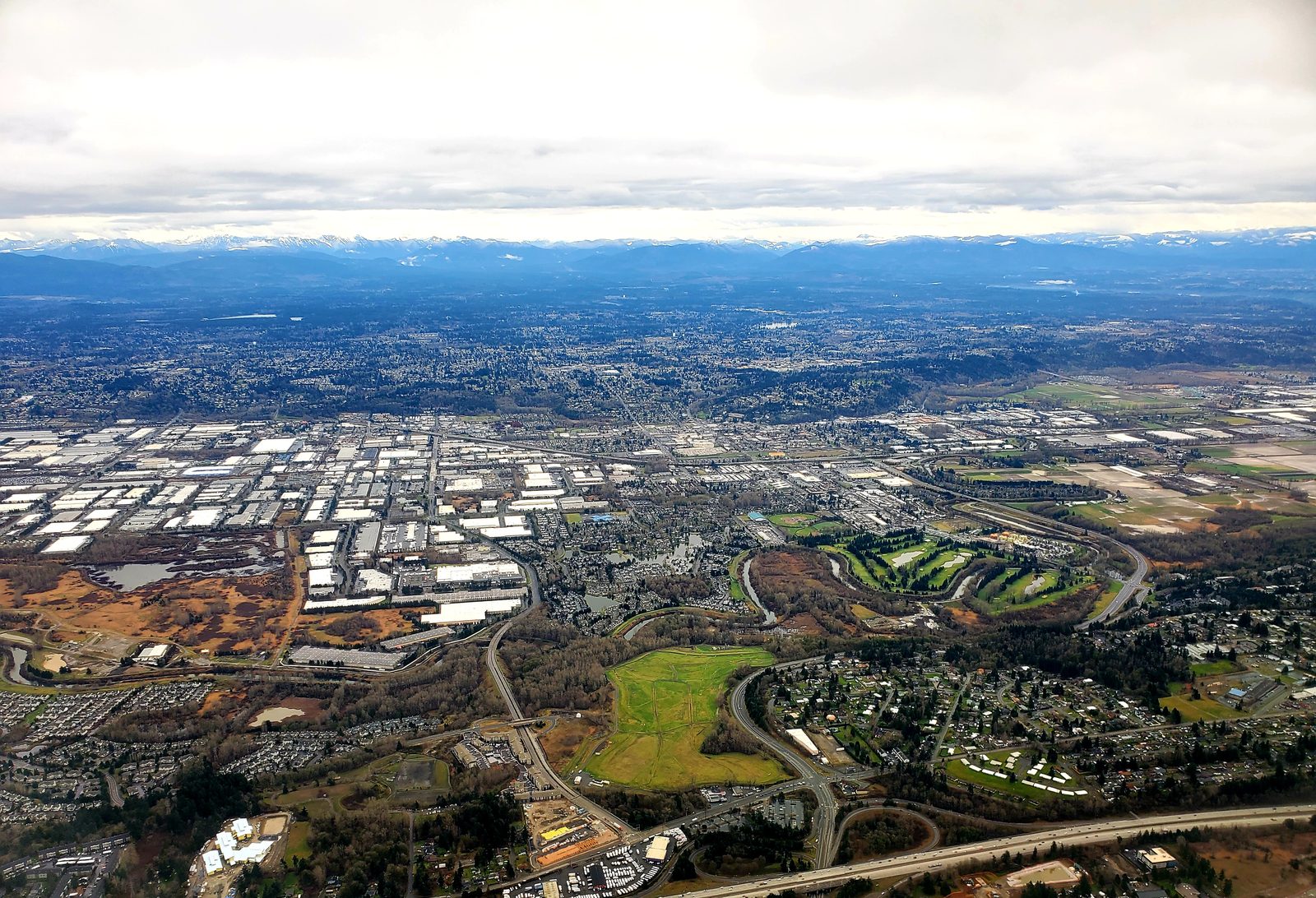 Aerial view of the Kent Valley: warehouses and manufacturing along the valley floor, neighborhoods rising on the hillsides, and the Cascade foothills beyond