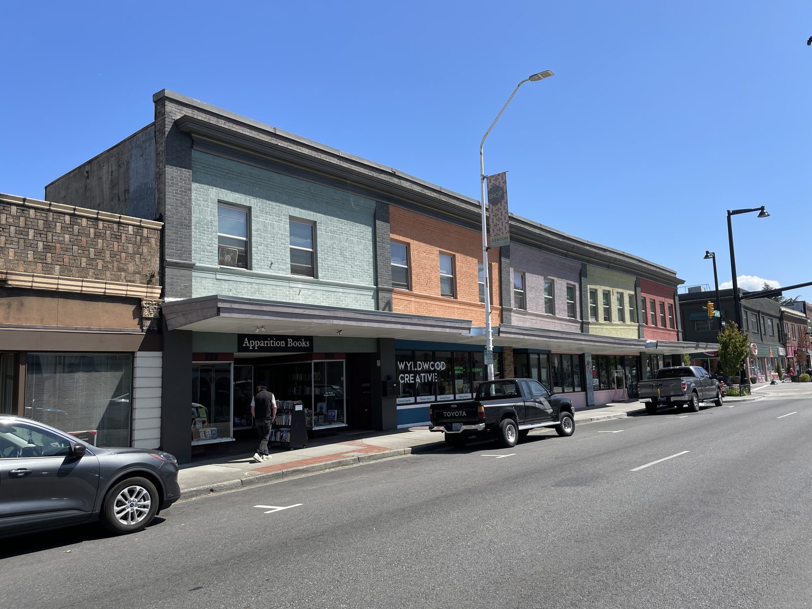 Painted brick storefronts along South 3rd Street in downtown Renton, with a shopper at the bookstore