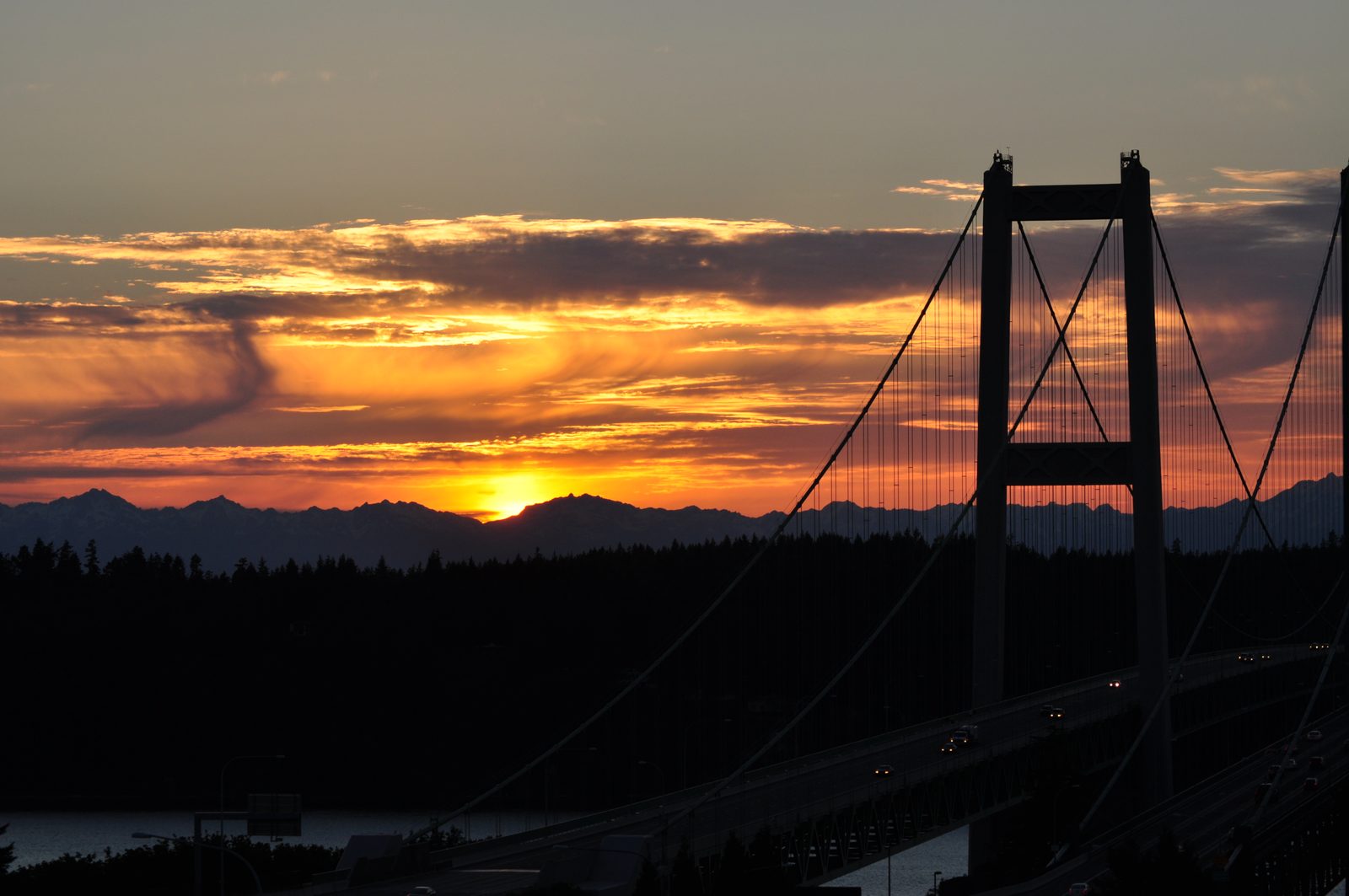 The Tacoma Narrows Bridge silhouetted at sunset, with the Olympic Mountains and Puget Sound behind it