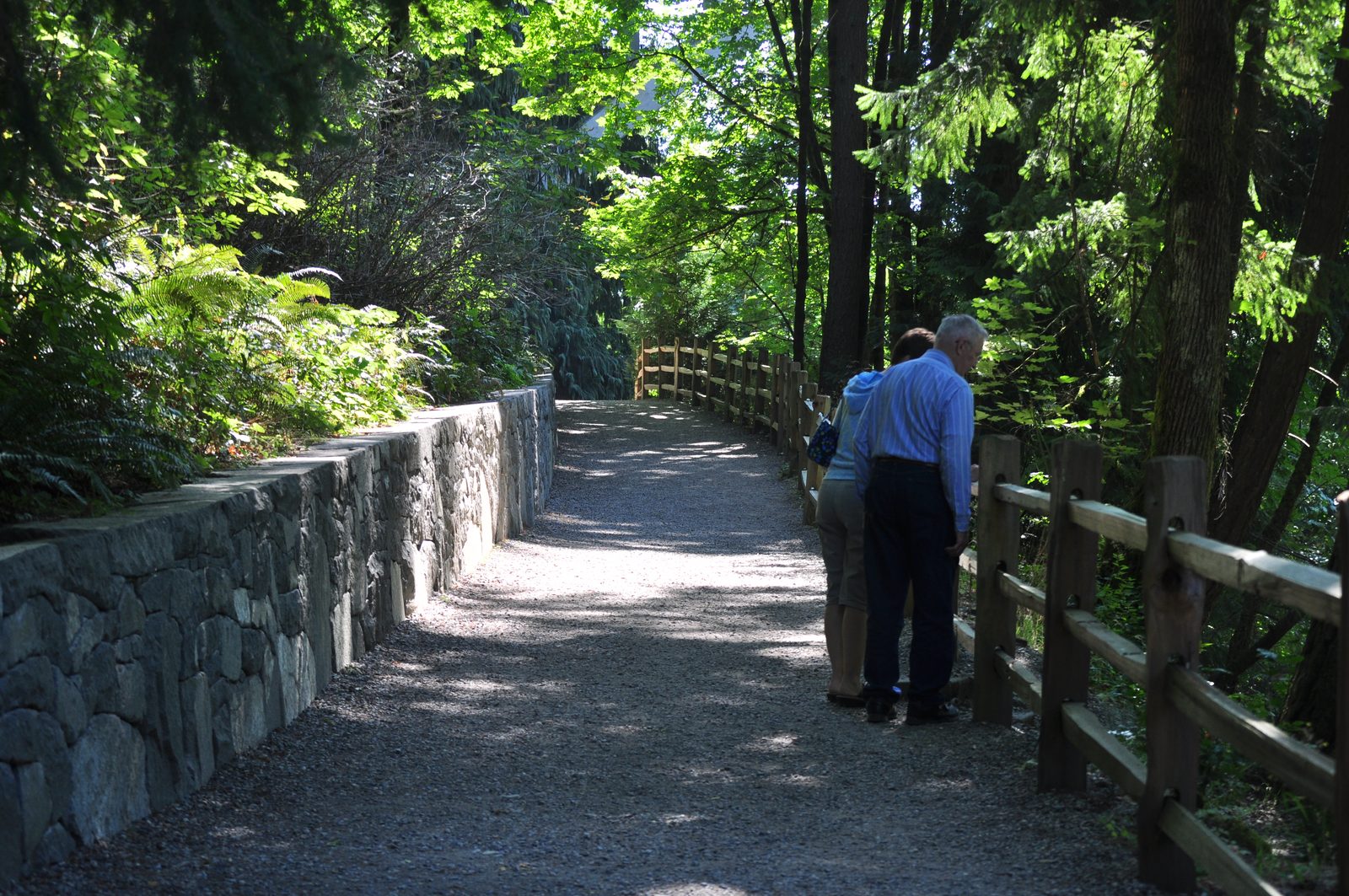 A couple walking the paved riverside trail along a stone retaining wall in Tumwater Falls Park, on the Deschutes River