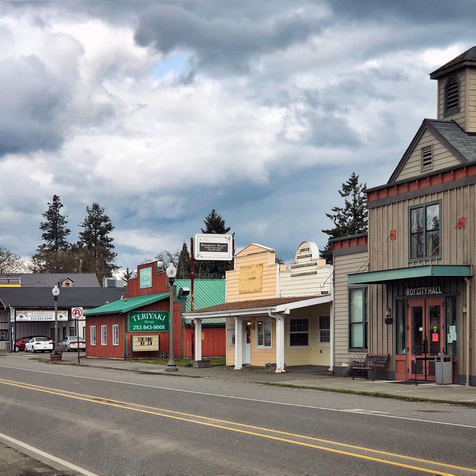 Wooden storefronts along McNaught Road, the main street of Roy, with the City Hall tower